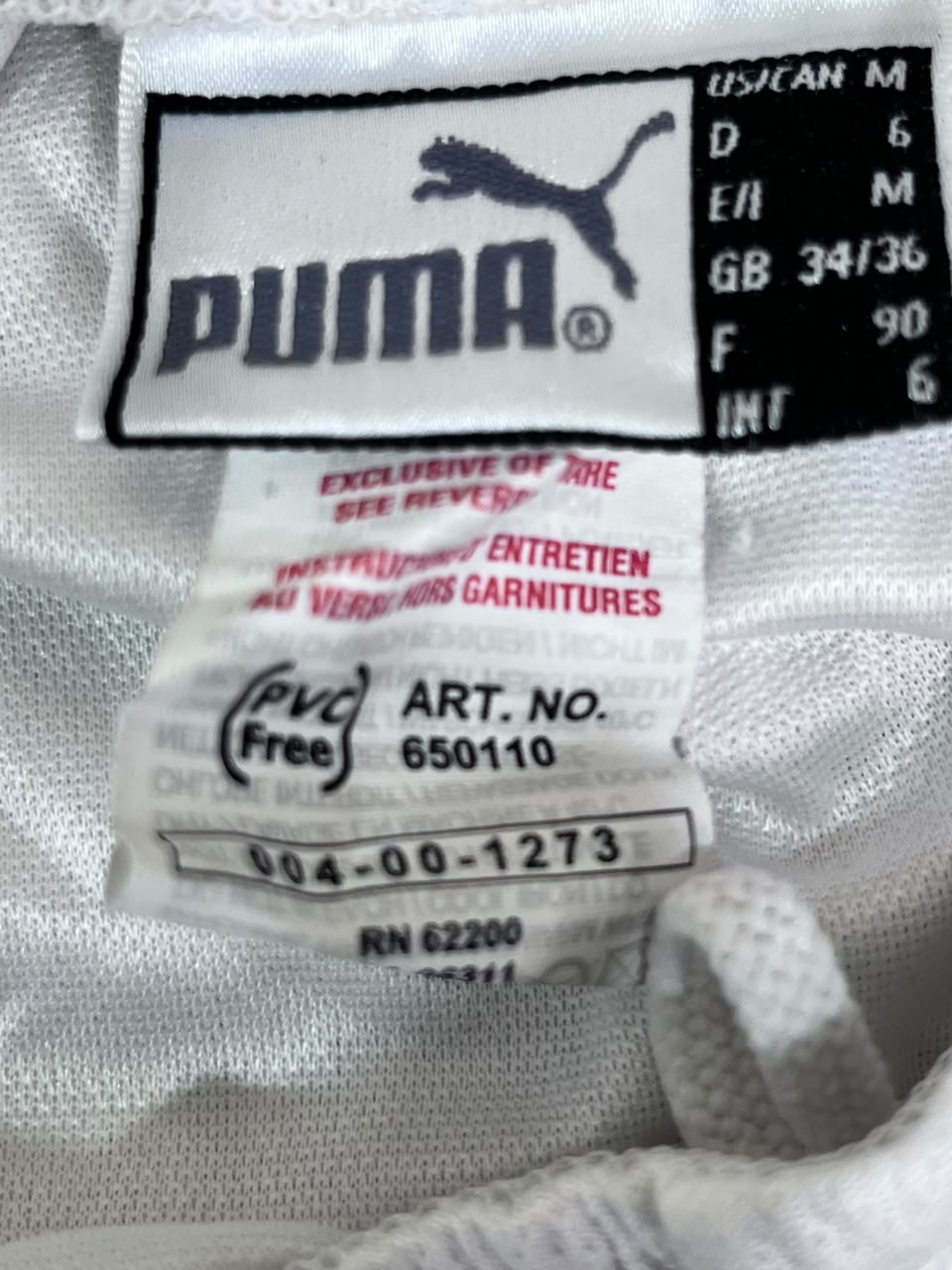 Close-up of a Puma garment label sewn onto white knit fabric, showing the Puma cat logo, size information, and care instructions.