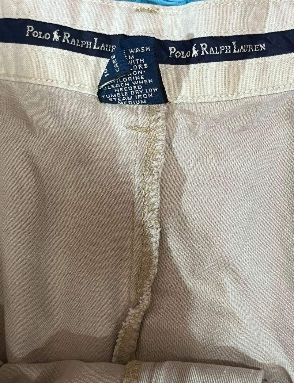 Close-up of Polo Ralph Lauren clothing showing the interior waistband, beige fabric, and dark navy brand labels sewn along the edge.