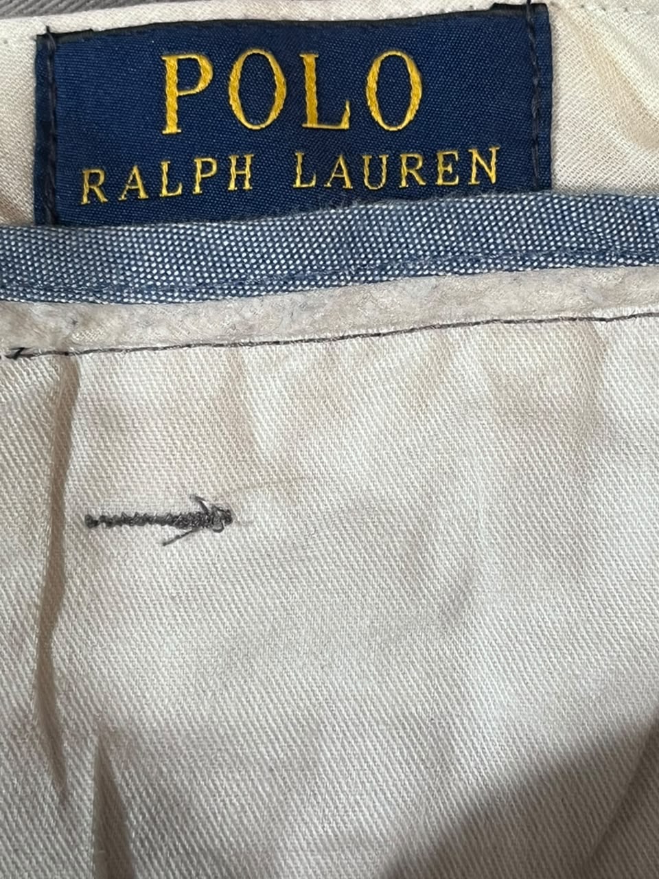 Close-up of Polo Ralph Lauren clothing showing the navy blue brand label with gold lettering and a light beige fabric body.