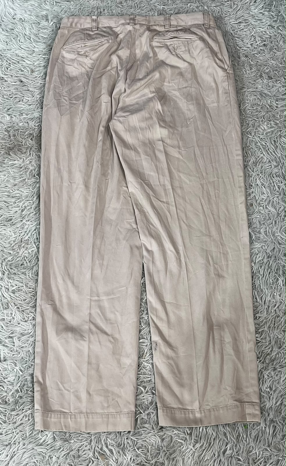 A pair of light beige or khaki trousers on the white background