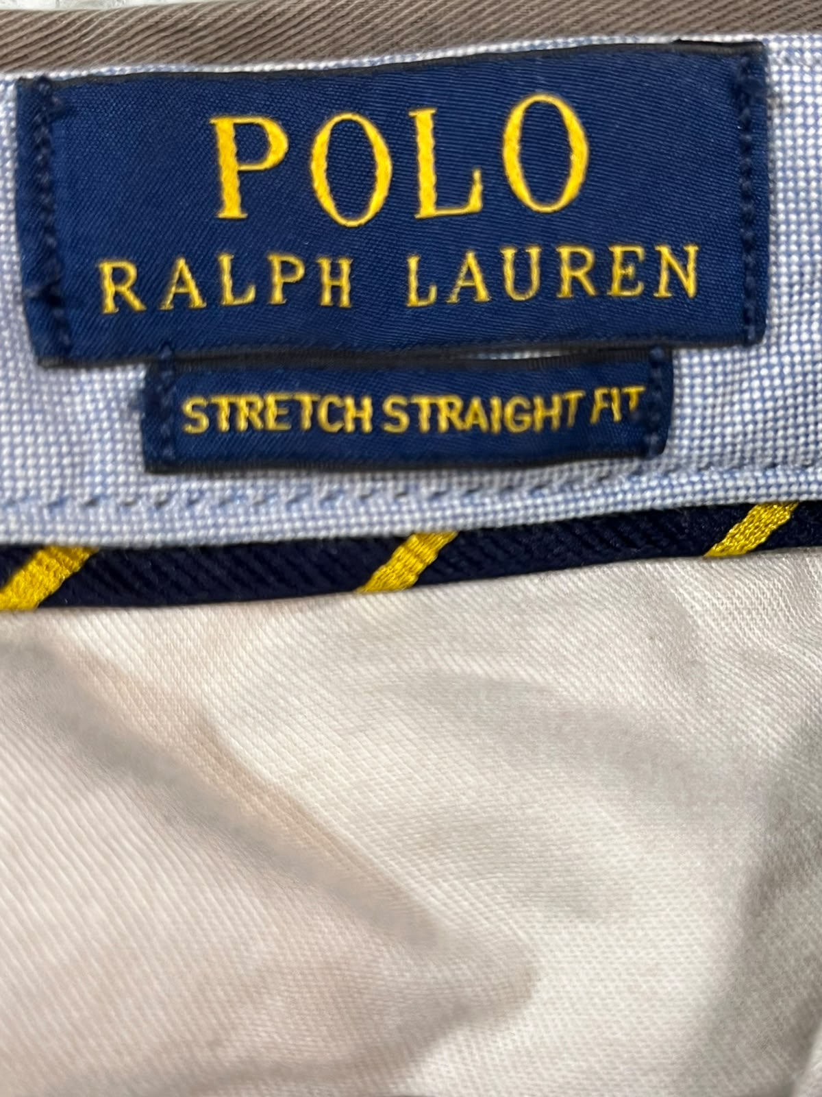 Close-up of a Polo Ralph Lauren garment label on a light-colored woven fabric, with navy blue labels and yellow lettering reading 'POLO RALPH LAUREN' and 'STRETCH STRAIGHT FIT'.