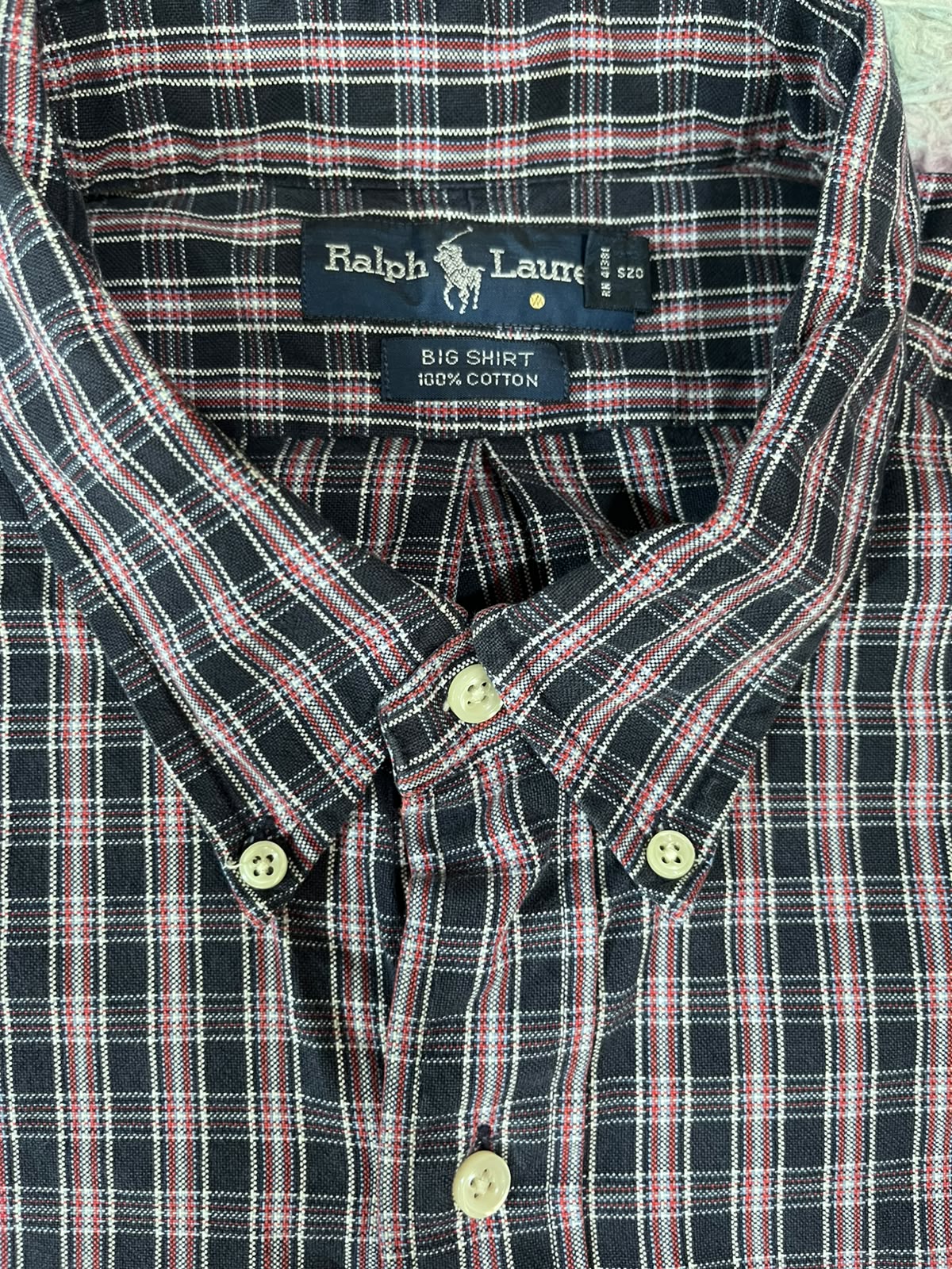 Close-up of a Ralph Lauren button-down shirt with a navy, red, and white plaid pattern, showing the inner neck label and front buttons.