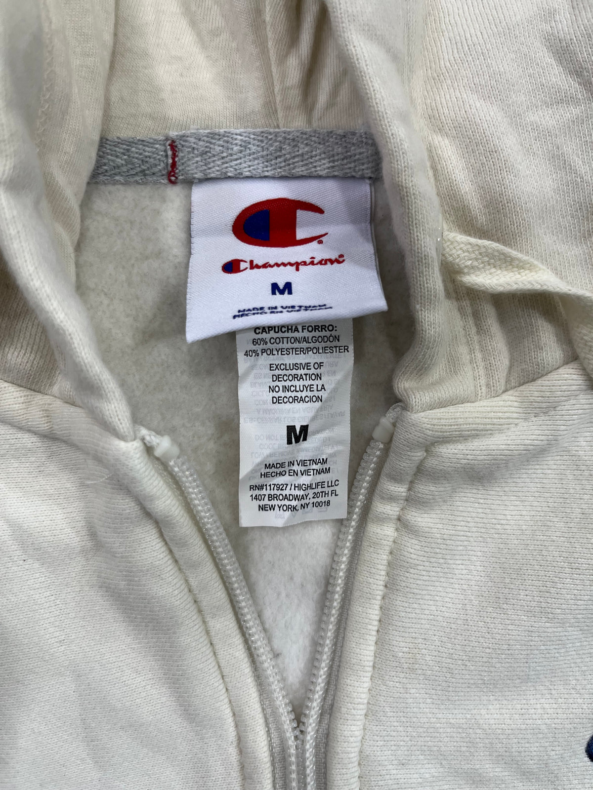 Close-up of a Champion garment interior showing the brand label and zipper area on a light beige fabric.