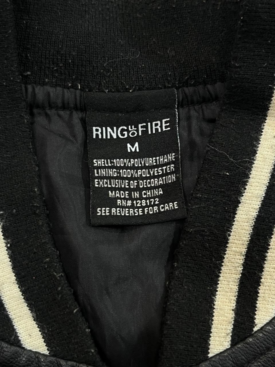 Close-up of the interior neck label of a black striped knit garment, showing the brand RING OF FIRE and size M.