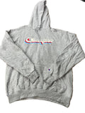 A heather gray Champion hoodie with a red, white, and blue embroidered logo on the chest, with other clothes visible in the background.