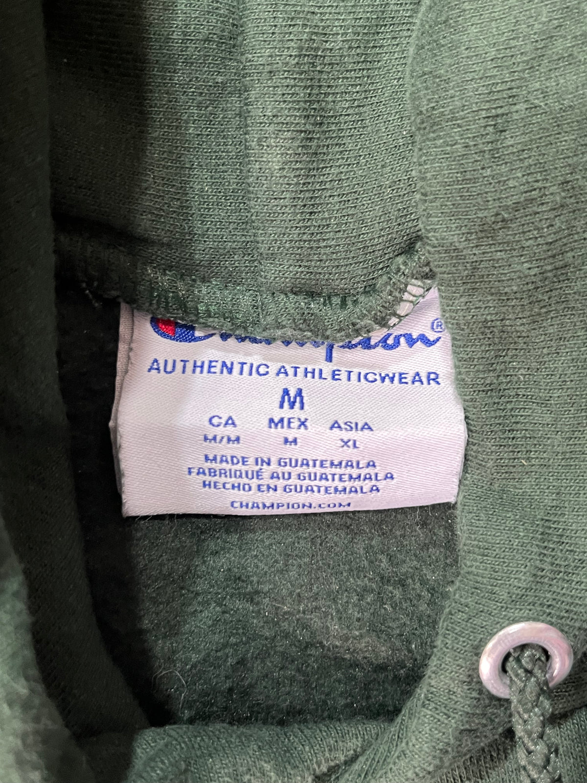 Close-up of a Champion athletic garment label sewn inside the collar of an olive green knit top, with size information visible.