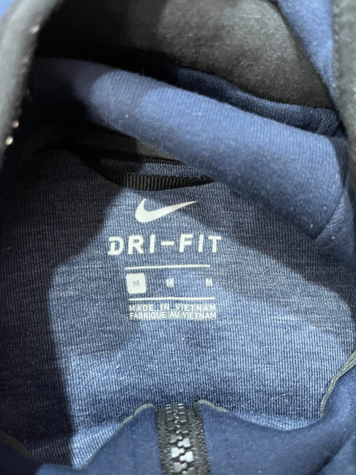 Close-up of the inside collar of a blue Nike garment, showing the white Nike Swoosh and DRI-FIT text printed on the lining.
