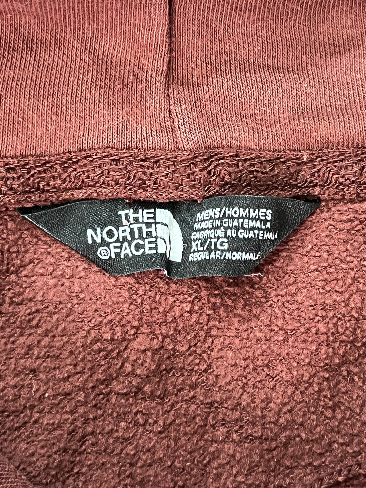Close-up of a terracotta-colored knit garment showing a black fabric brand label for The North Face.