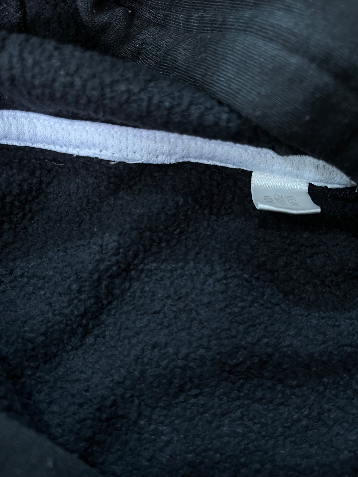 Close-up of a black fleece or sherpa-lined garment with a white trim strip and a small white fabric tag attached.