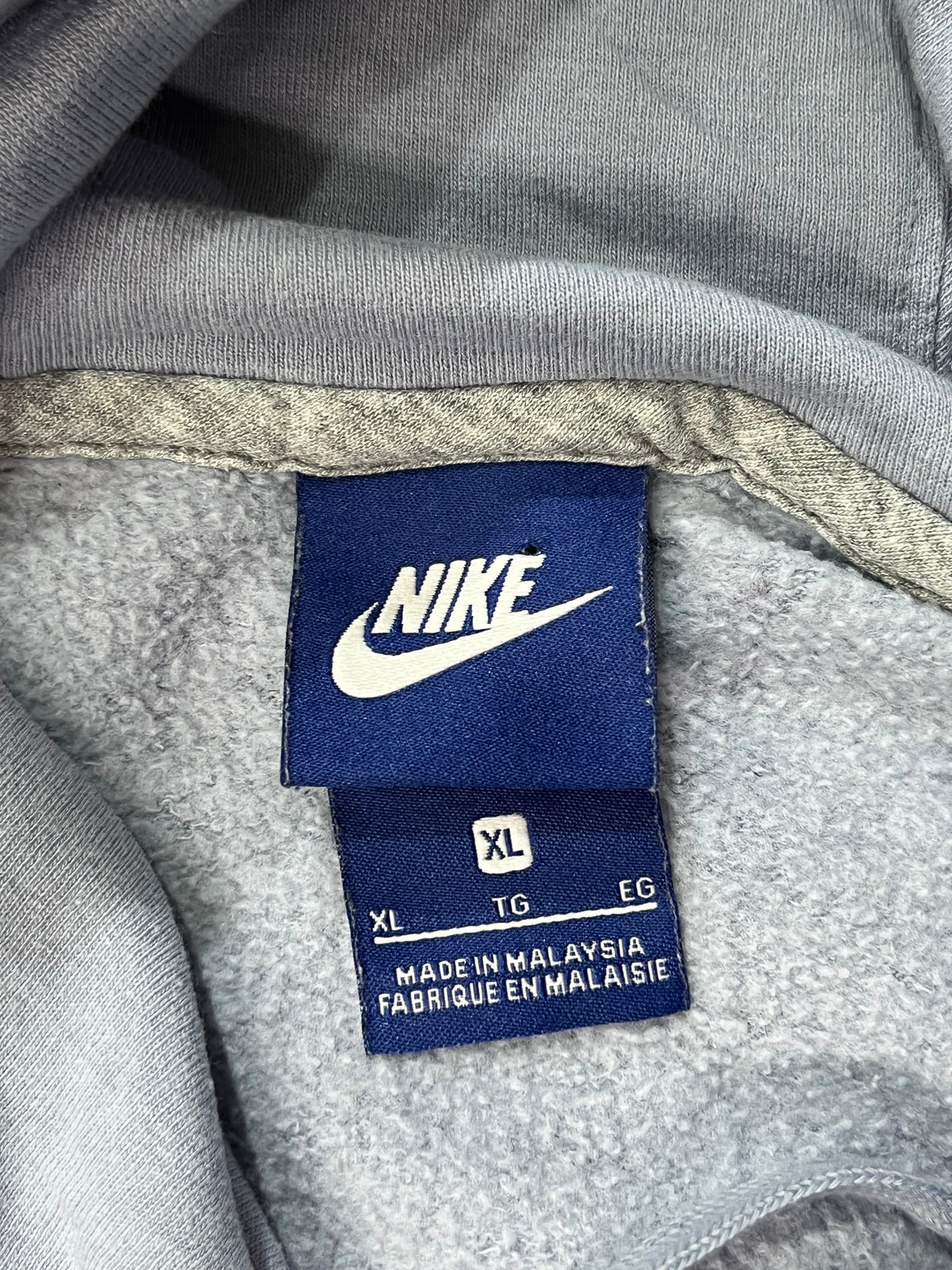 Close-up of a gray Nike hoodie interior showing the blue Nike brand tag with white logo and size information.