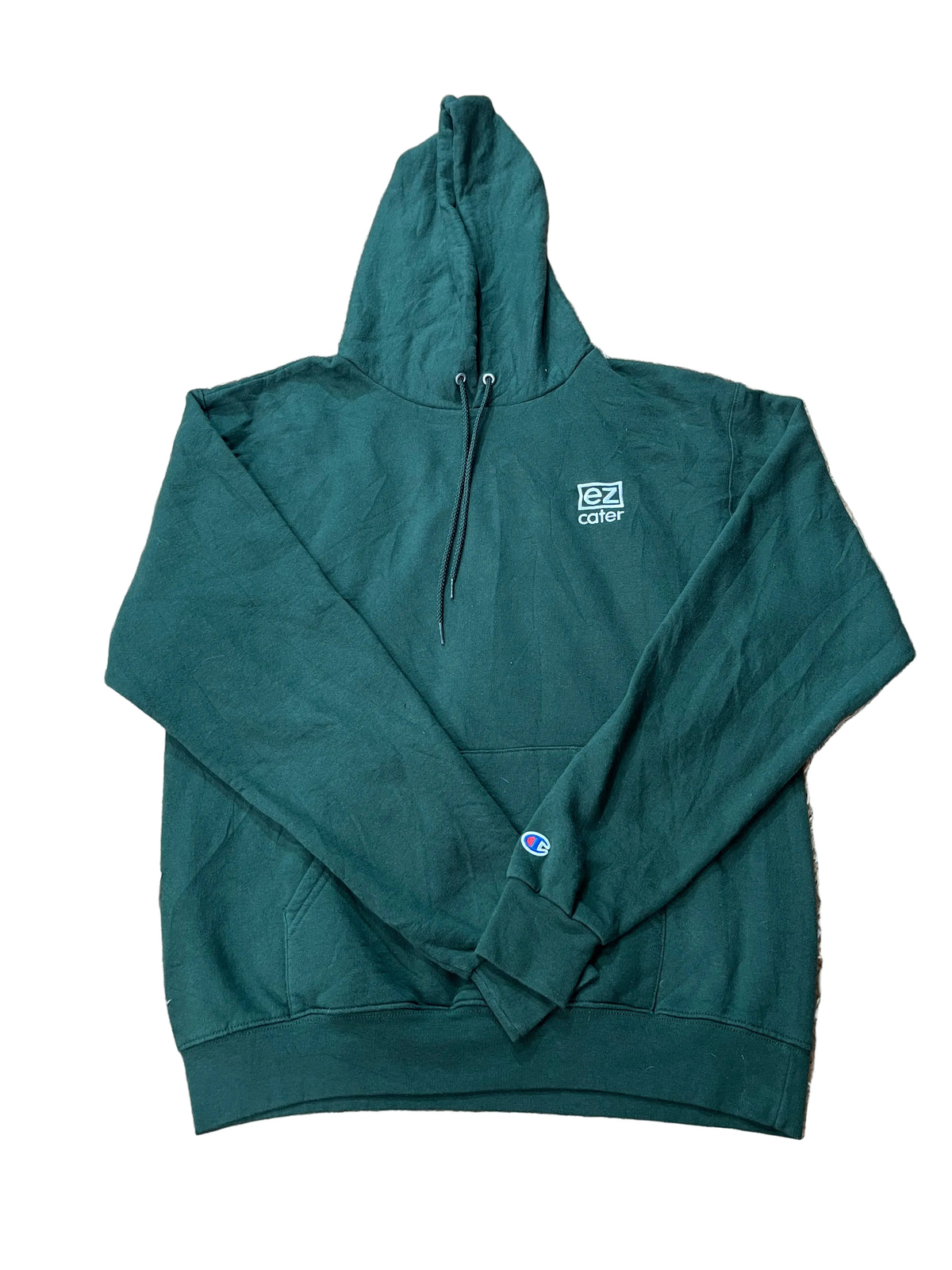 A dark green Champion pullover hoodie with a small white chest logo and a blue/red Champion emblem on the left sleeve, 