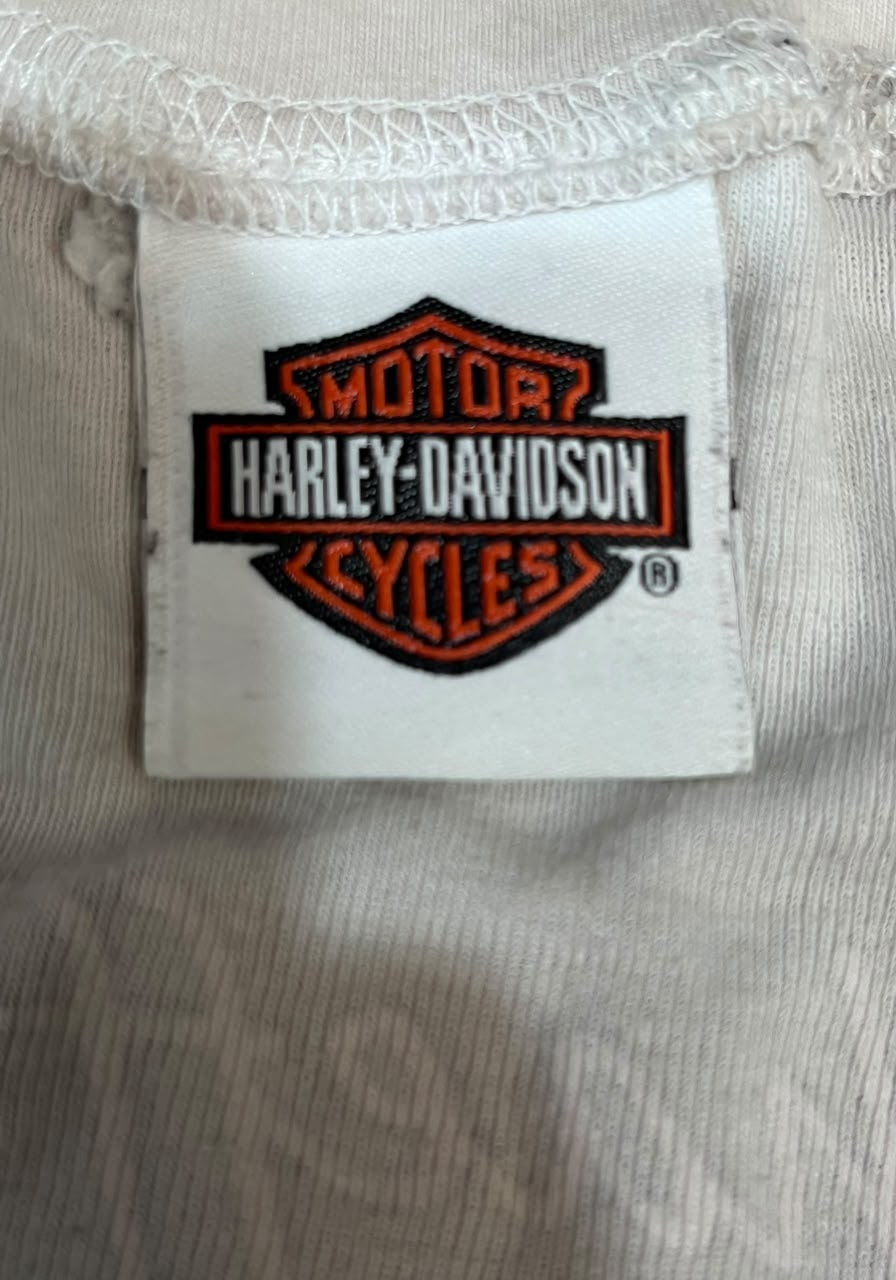 Close-up of a Harley-Davidson brand sewn-in label on a white ribbed knit garment, showing the embroidered orange and black logo on a white fabric patch.