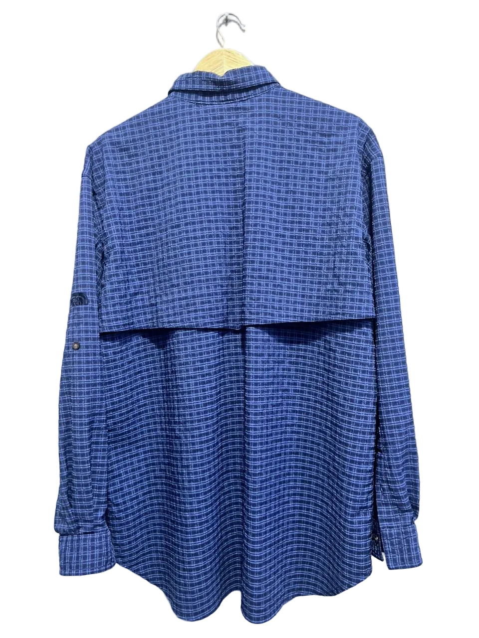 The north face blue checkered shirt on a hanger against a white wall