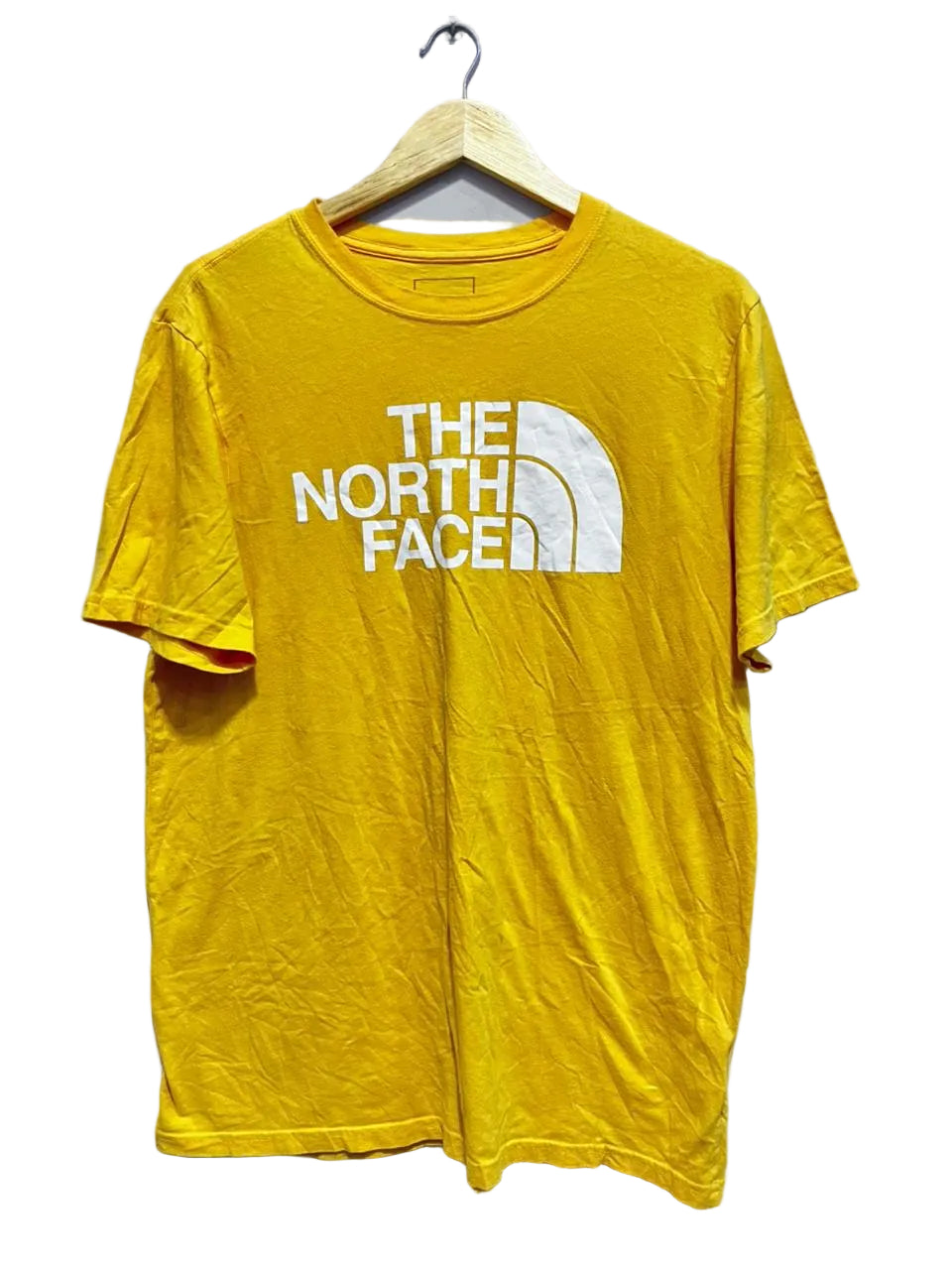 Yellow t-shirt with The North Face logo on a hanger against a white wall.