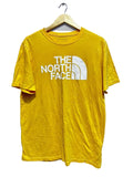 Yellow t-shirt with The North Face logo on a hanger against a white wall.