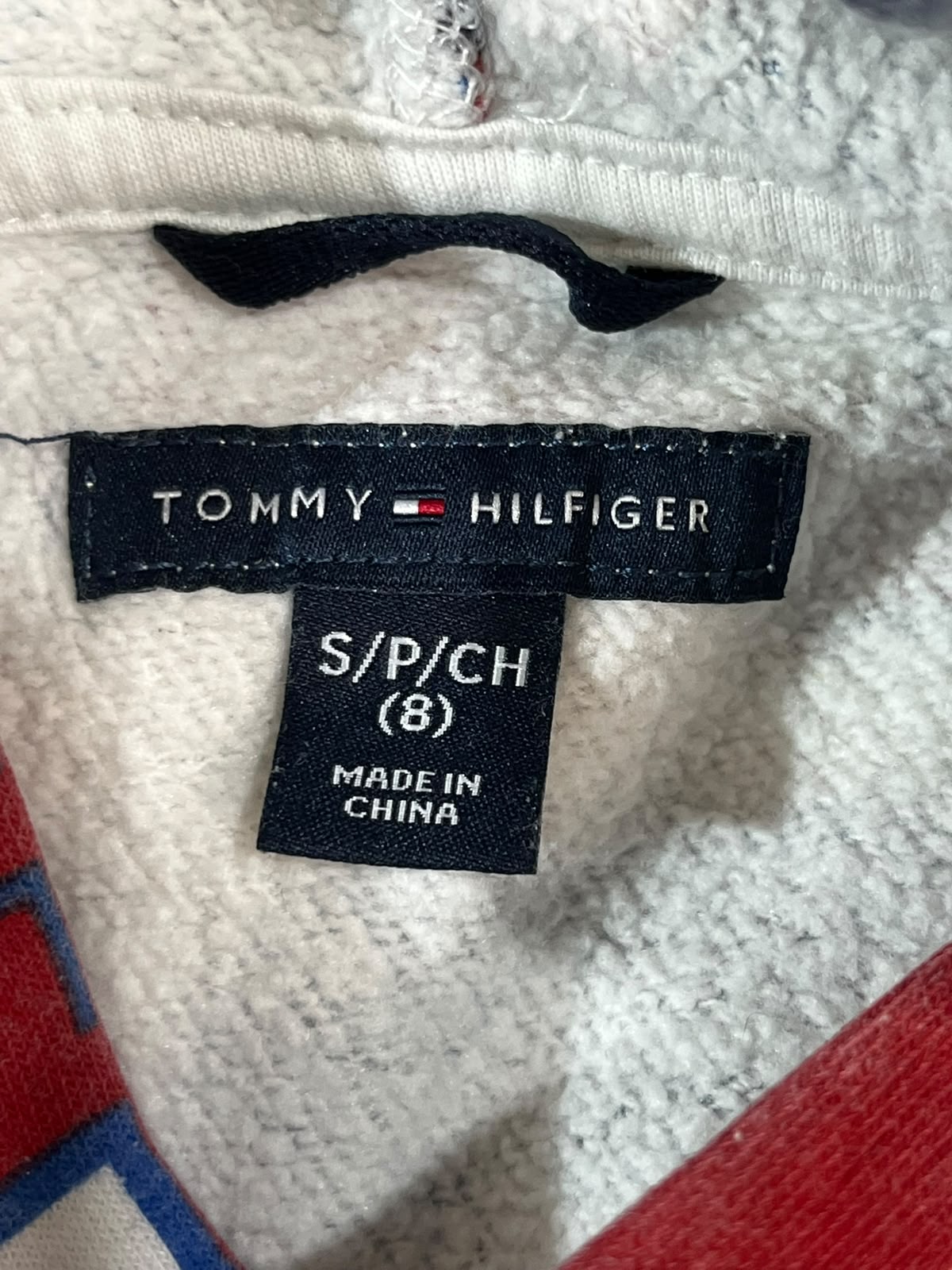 Close-up of a Tommy Hilfiger garment interior label on a textured white fabric, with size text 'S/P/CH (8)' and 'MADE IN CHINA' visible.