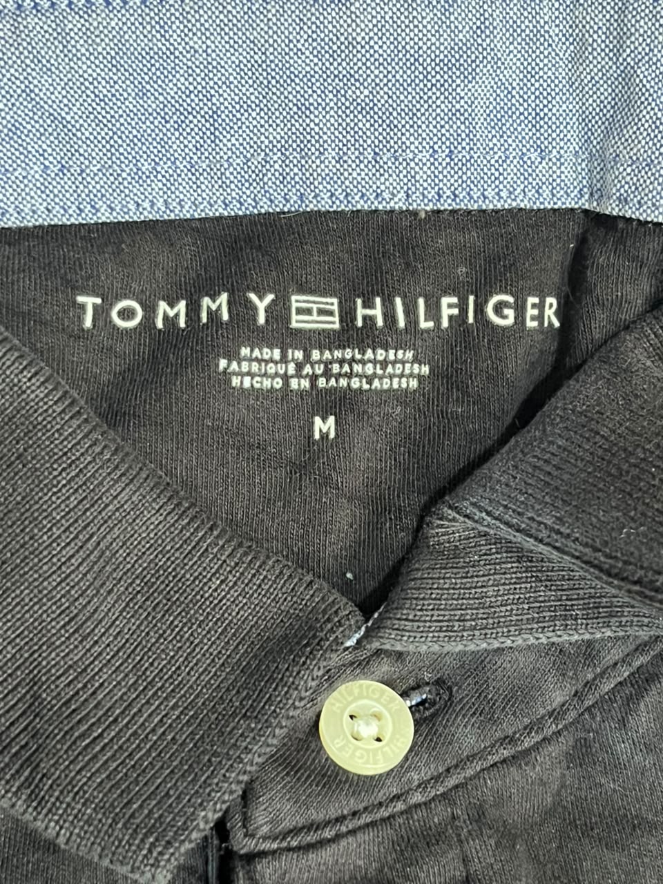 Close-up of a Tommy Hilfiger polo shirt collar showing the black inner neck label with white branding text and a light-colored button.