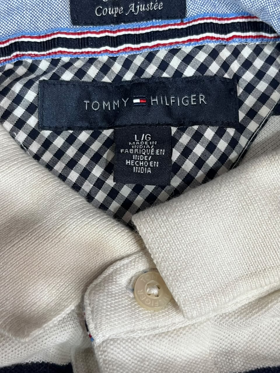 Close-up of a Tommy Hilfiger polo shirt collar showing the black and white gingham pattern lining, navy brand label, and cream-colored knit fabric.