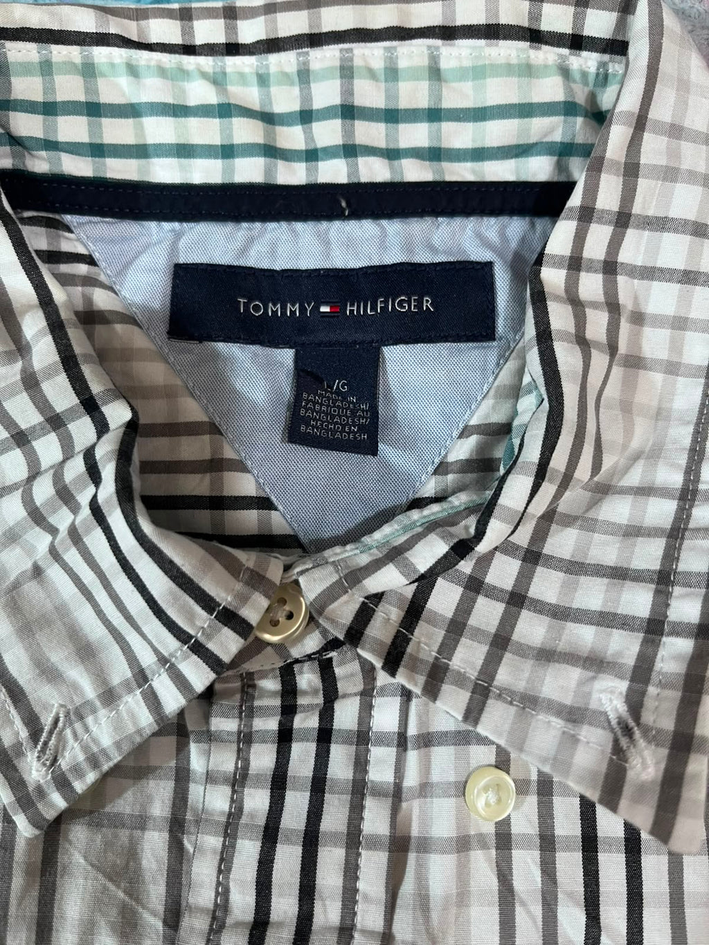 Close-up of a Tommy Hilfiger plaid button-down shirt collar, showing the brand label and the pattern of black, white, and green stripes.