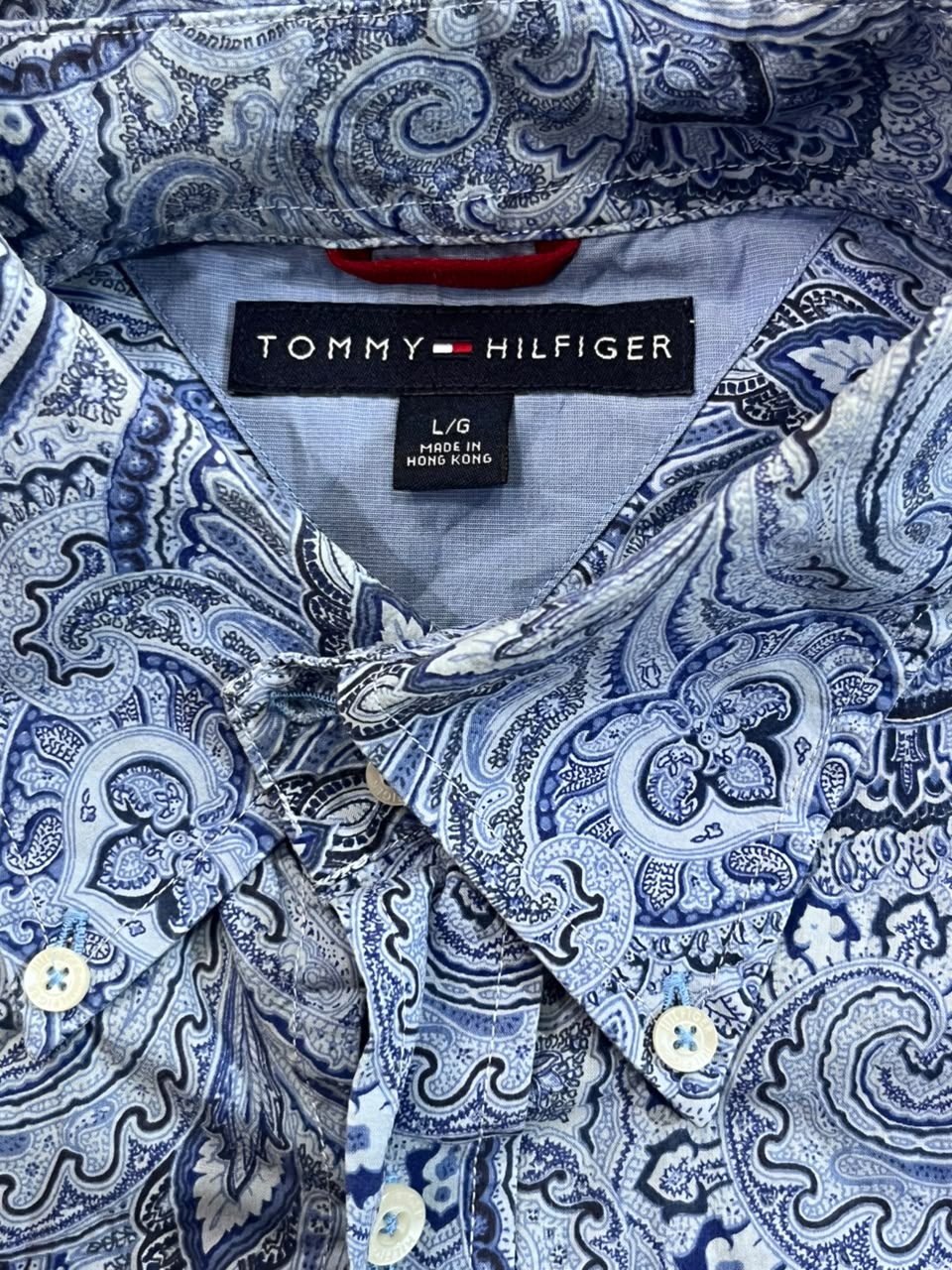 Close-up of a Tommy Hilfiger button-down shirt with a blue and white paisley pattern, showing the inner collar and brand label.