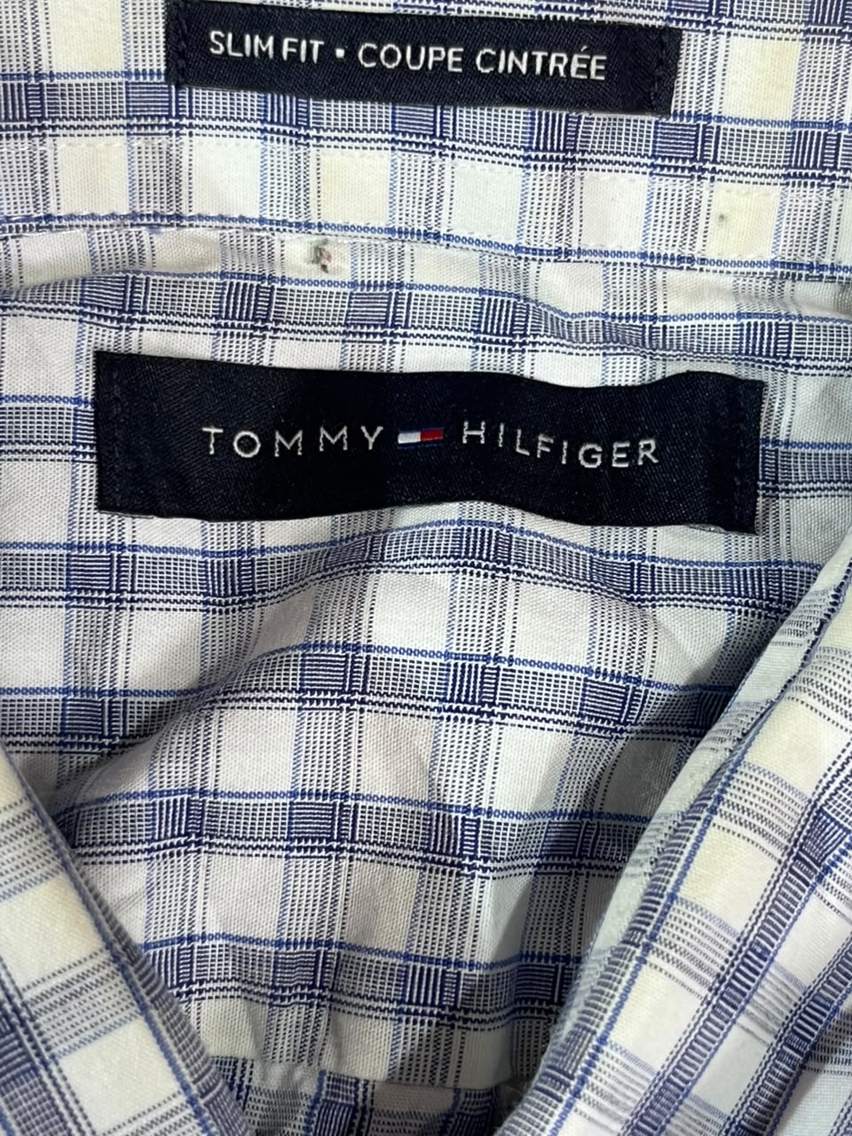 Close-up of a Tommy Hilfiger plaid shirt lining with a black brand label and size label reading Slim Fit / Coupe Cintrée.