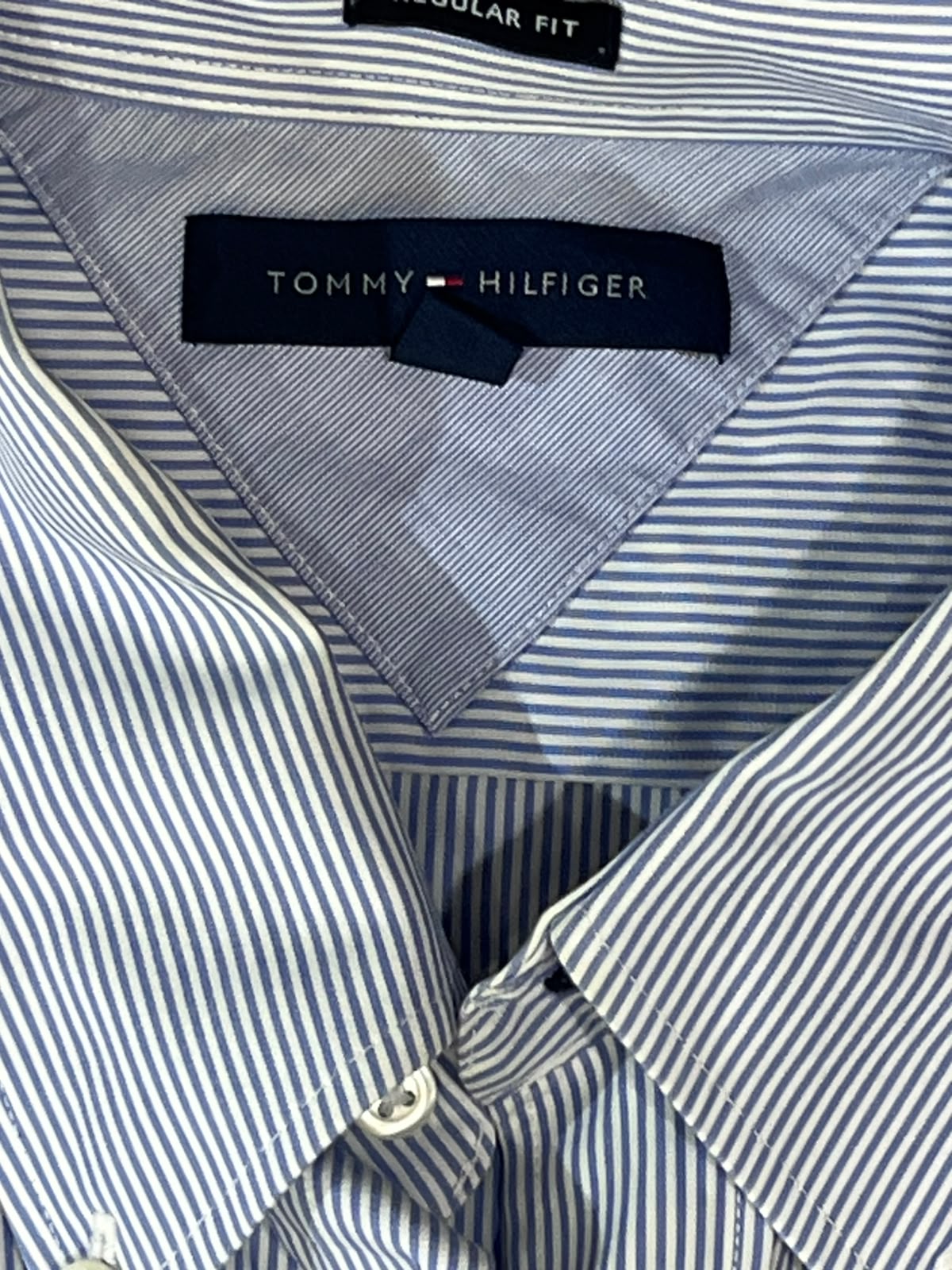Close-up of a Tommy Hilfiger striped dress shirt collar showing the navy brand label and blue and white pinstriped fabric.