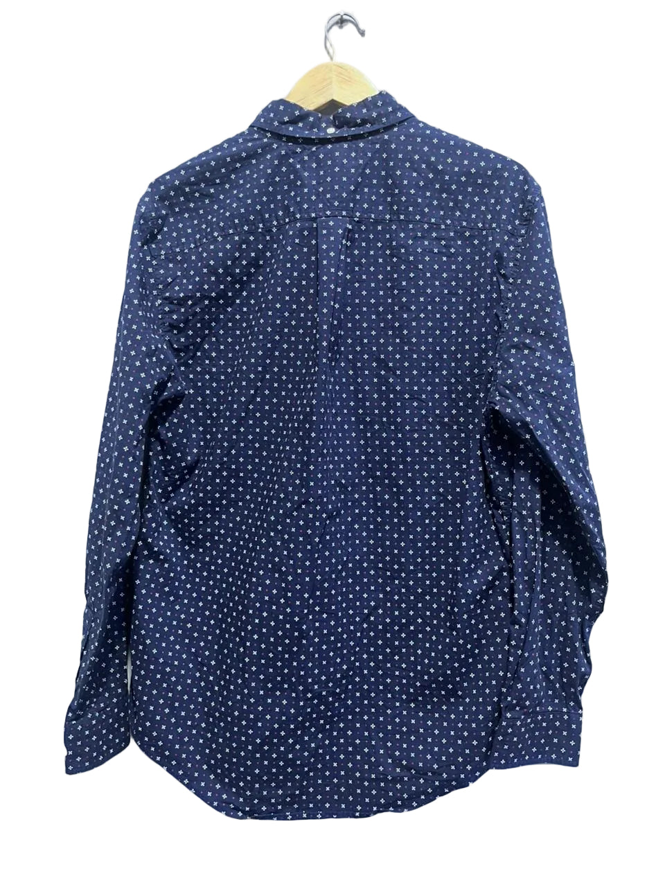 Navy blue shirt with white polka dots on a hanger against a white wall.