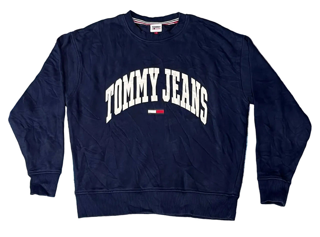 A navy blue crewneck sweatshirt with 'TOMMY JEANS' printed in white arched letters and a small red, white, and blue flag logo on the chest