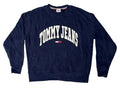 A navy blue crewneck sweatshirt with 'TOMMY JEANS' printed in white arched letters and a small red, white, and blue flag logo on the chest