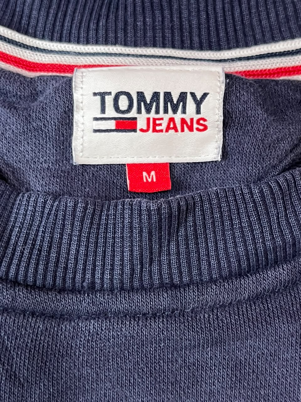 Close-up of a navy blue ribbed knit garment showing the Tommy Jeans neck label with red and white trim.
