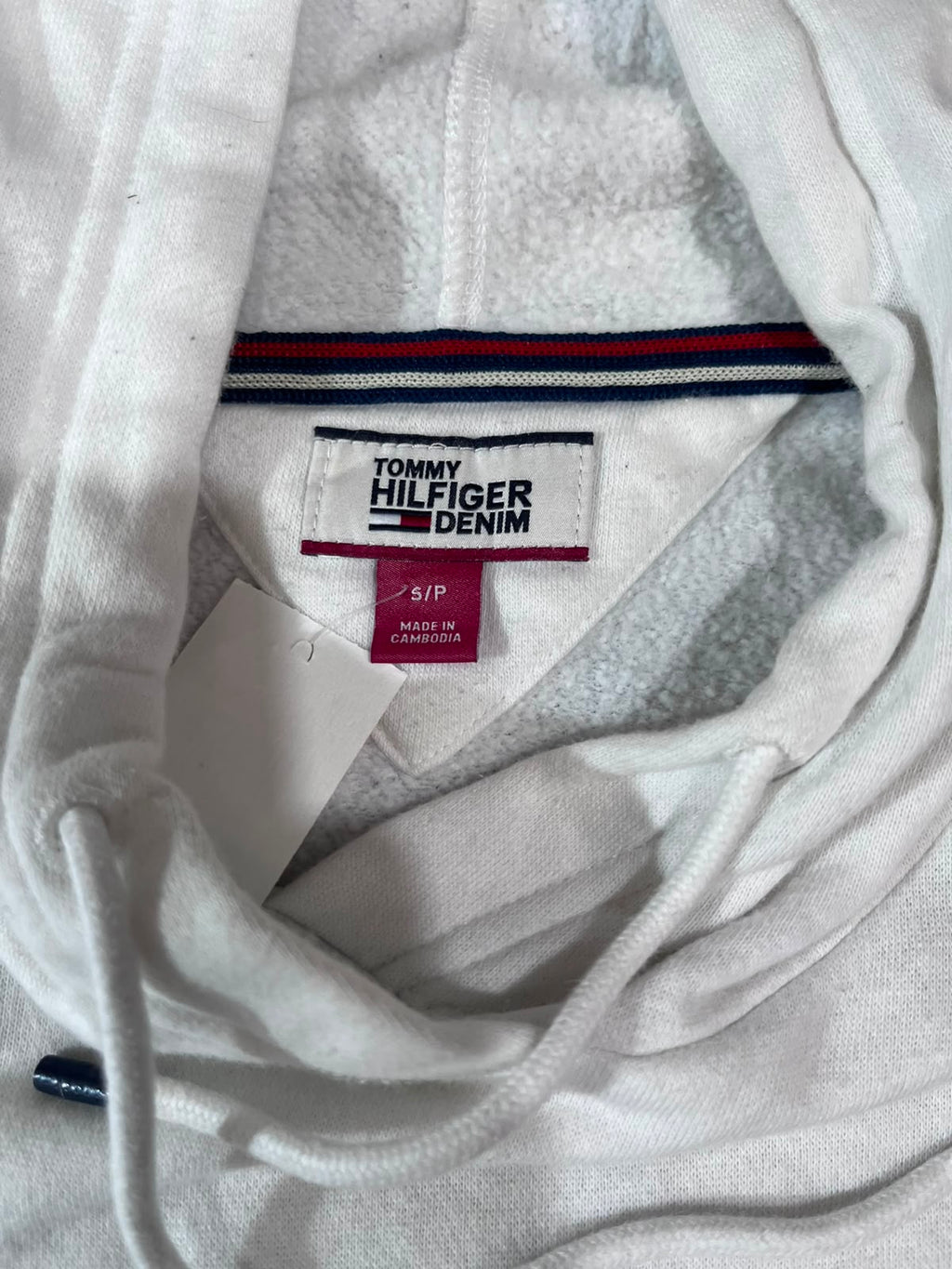 Close-up of a white Tommy Hilfiger Denim hoodie showing the inner neck label, drawstrings, and striped trim inside the collar.