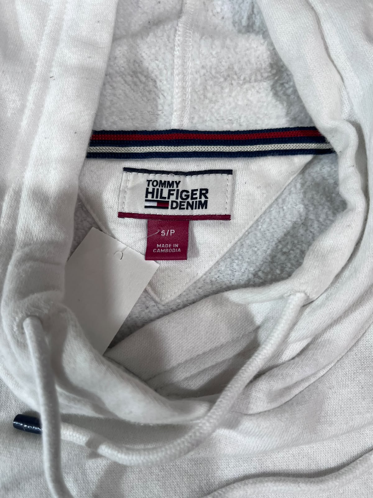 Close-up of a white Tommy Hilfiger Denim hoodie showing the inner neck label, drawstrings, and striped trim inside the collar.