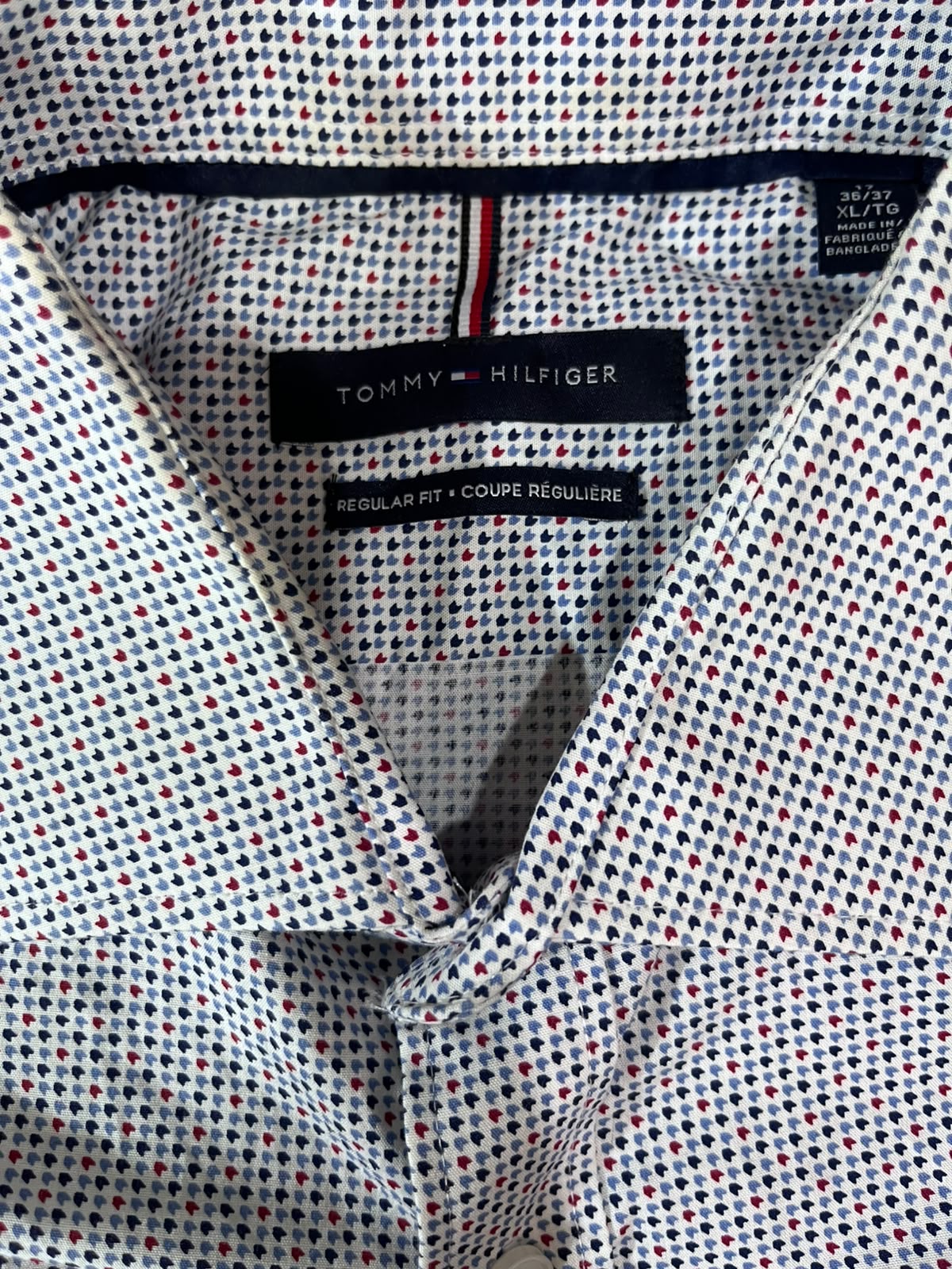 Close-up of a Tommy Hilfiger button-down shirt collar showing the brand label and a micro-checkered pattern of navy, red, and white dots.