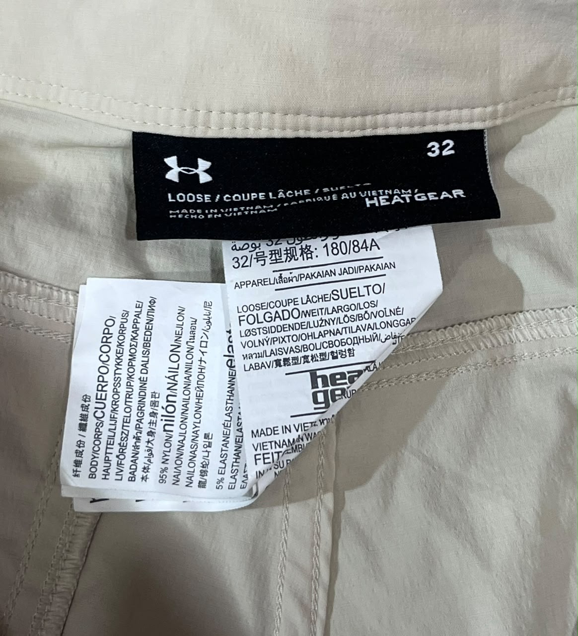 Close-up of a garment's interior labels showing the Under Armour brand tag and care instructions tag on off-white fabric.