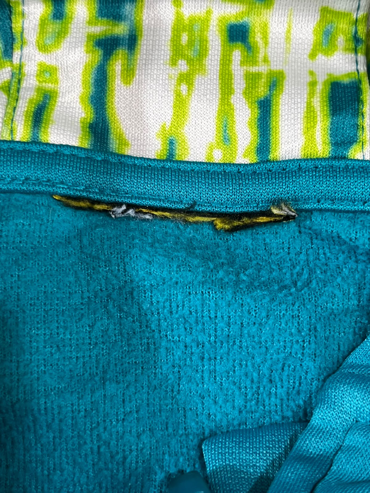 Close-up of a turquoise blue knit garment with a patterned white and lime green top section and a small yellow trim detail.