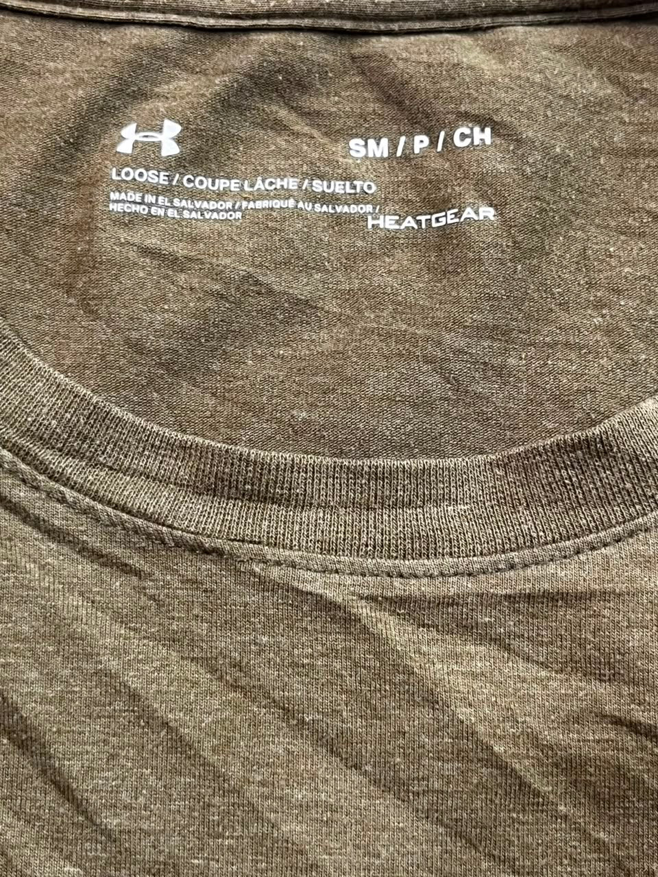 Close-up of the inside collar of a brown heathered t-shirt showing printed white text with Under Armour and Heatgear logos, size information, and country of origin.