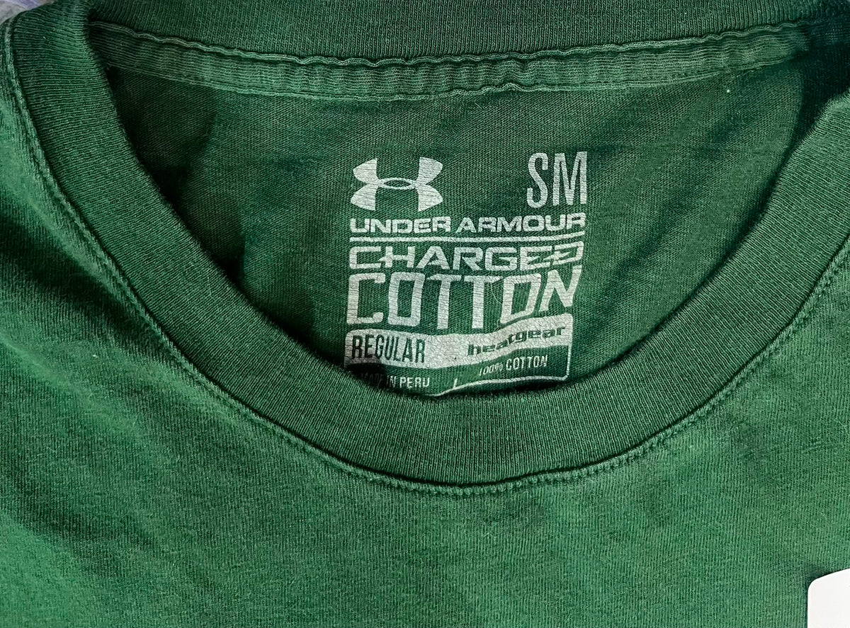 Close-up of the inside neck label of a dark green Under Armour Charged Cotton T-shirt, showing the Under Armour logo and size information.