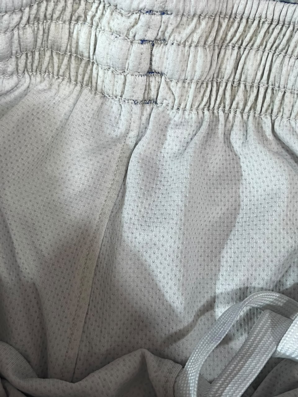 Close-up of light gray athletic shorts showing the textured mesh fabric and elastic waistband.