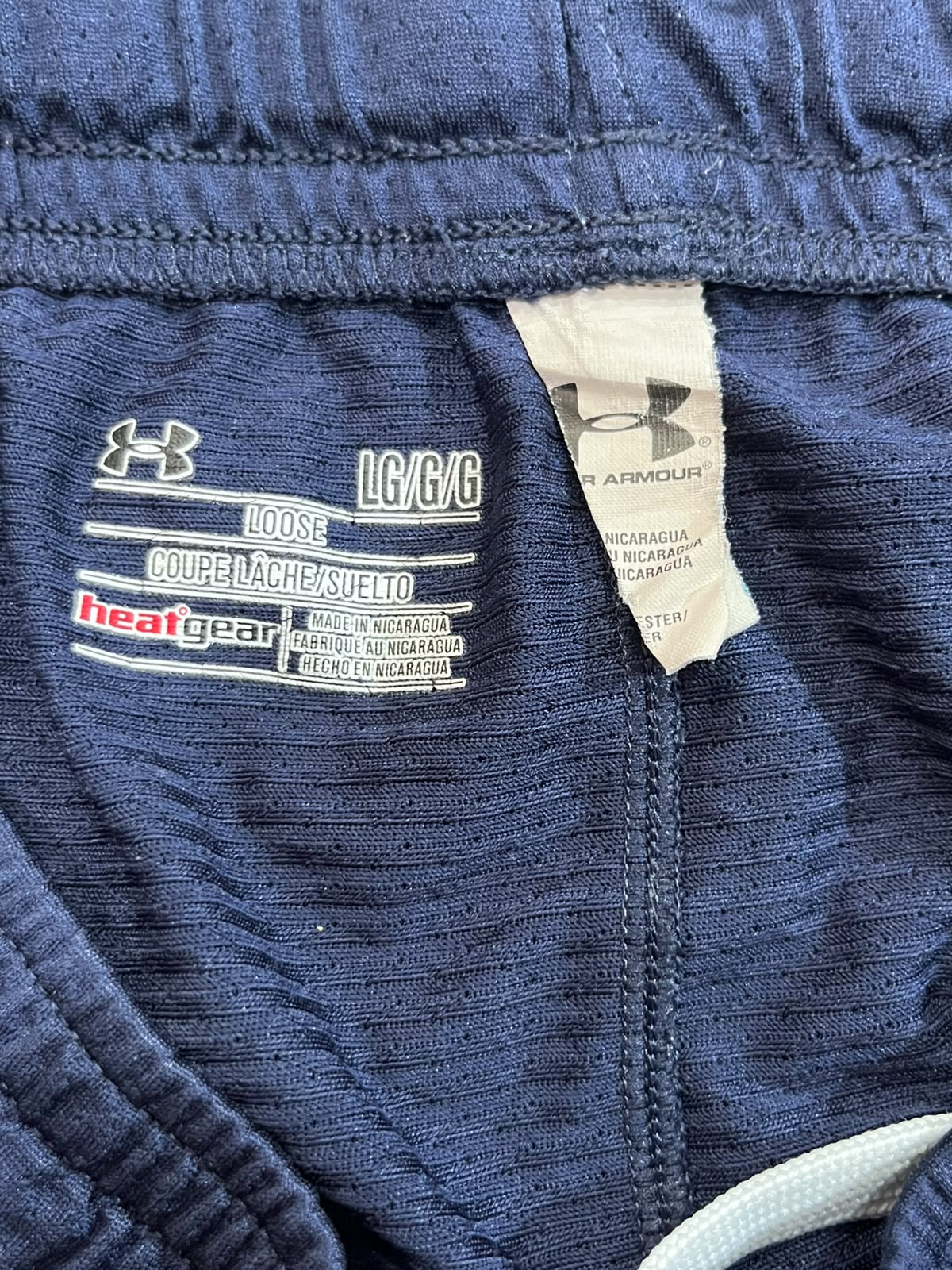Close-up of the inside waistband of Under Armour athletic pants in navy blue, showing the white Under Armour logo, size label 'LC/C/6', and a beige care tag.