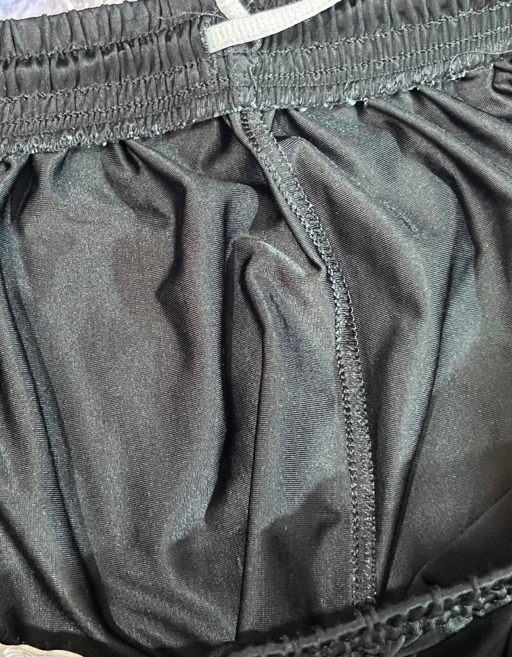 Close-up of dark gray athletic shorts showing the elastic waistband, center seam, and fabric texture.