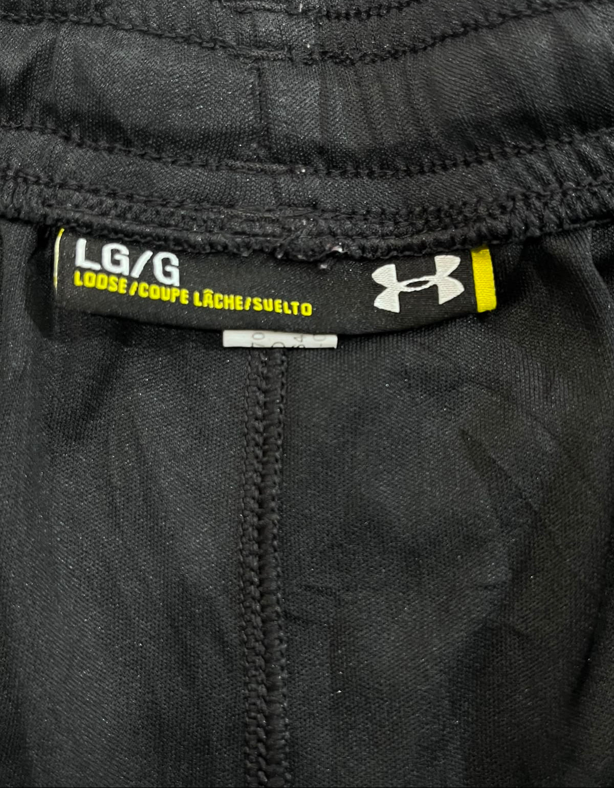 Close-up of the waistband of black Under Armour pants, showing the size label 'LG/G' and the Under Armour logo.