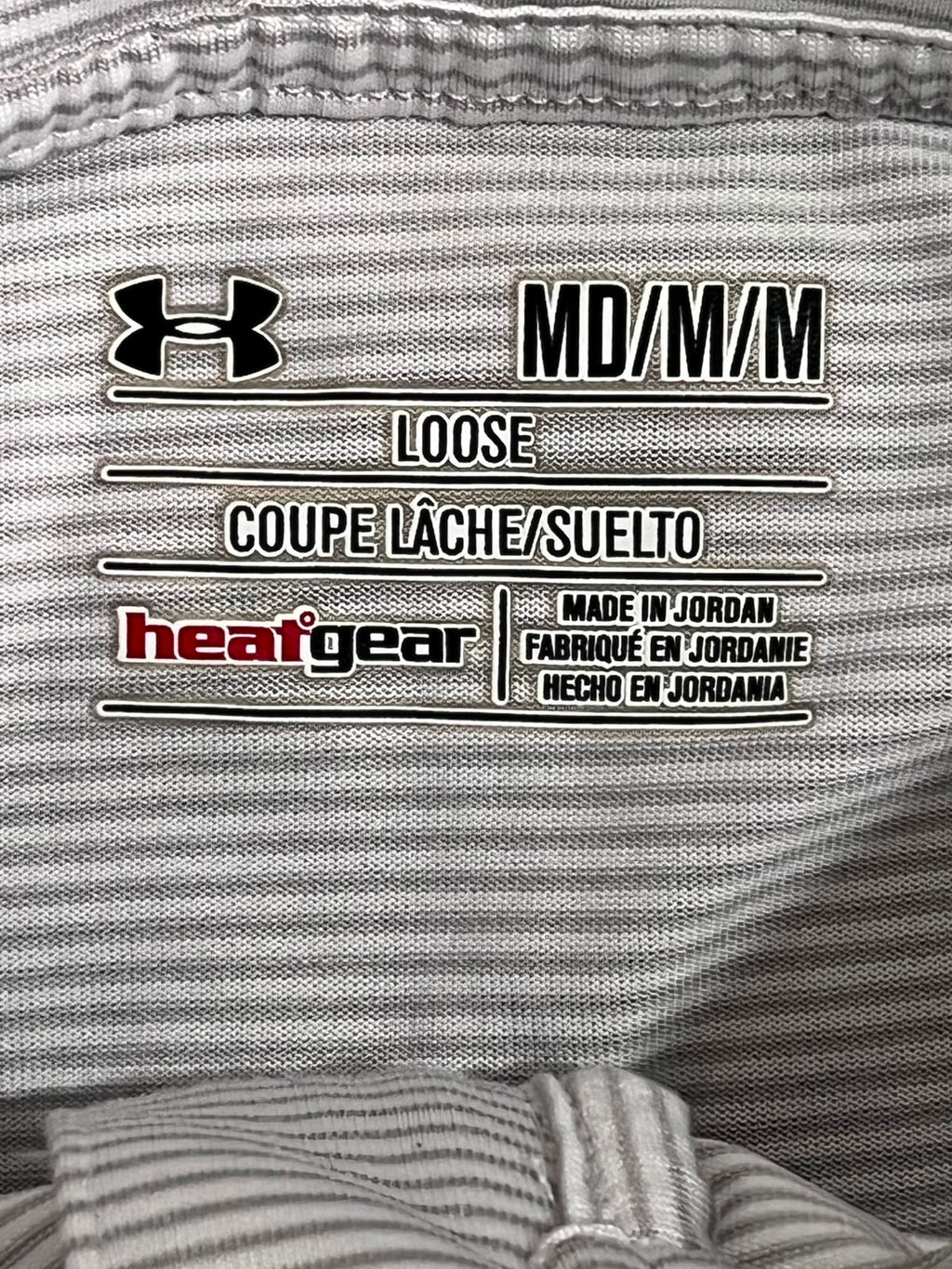 Close-up of a gray striped athletic garment label with the Under Armour logo, 'MD/M/M', 'LOOSE', and 'heatgear' branding.