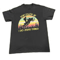 A black short-sleeve graphic t-shirt  The shirt features a retro-style circular sunset graphic with a snowmobile silhouette and the text 'DON'T FOLLOW ME' above and 'I DO STUPID THINGS' below in yellow.
