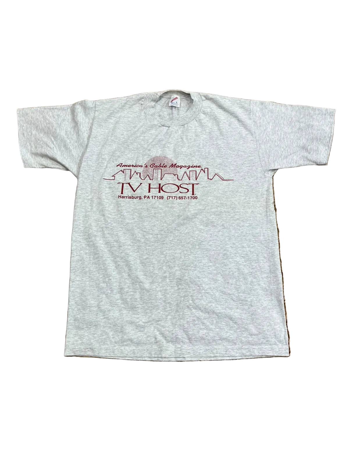 A light heather gray t-shirt with a maroon graphic print reading 'American & Canadian Magazine TV HOST' and 'Patterson, P.A.