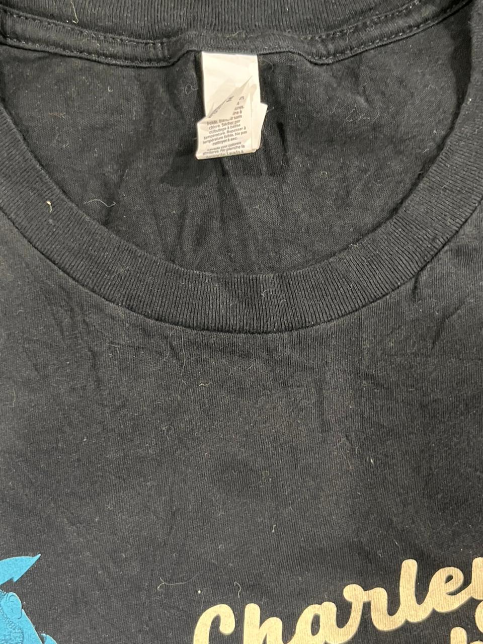 Close-up of a black t-shirt neck area showing a white care tag and part of a yellow graphic print reading 'Charle'.