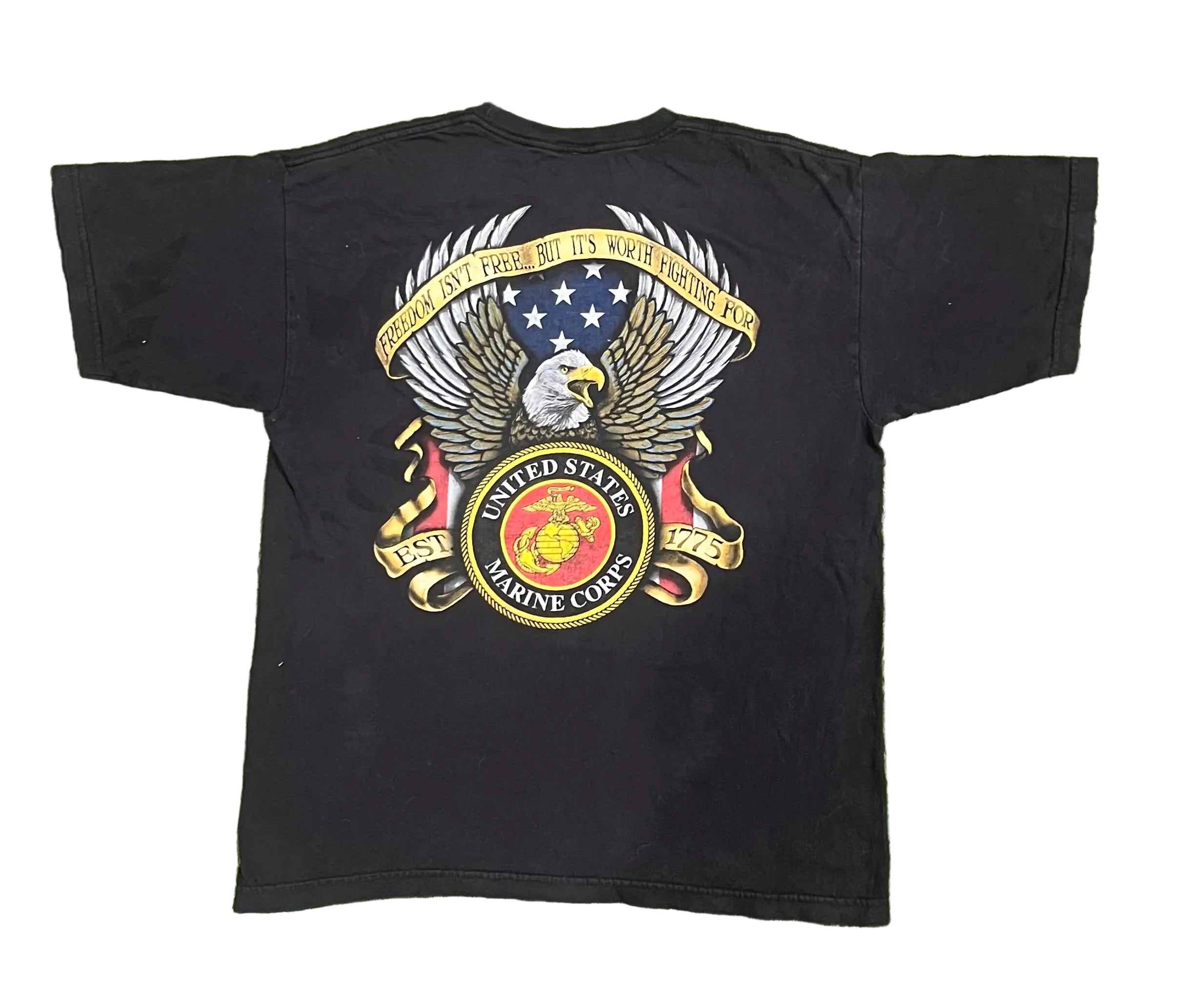 A black short-sleeve t-shirt laid flat showing a large back graphic of the United States Marine Corps emblem with an eagle, shield, and anchor, and banners reading 'United States Marine Corps' and 'God Is Proud.'.