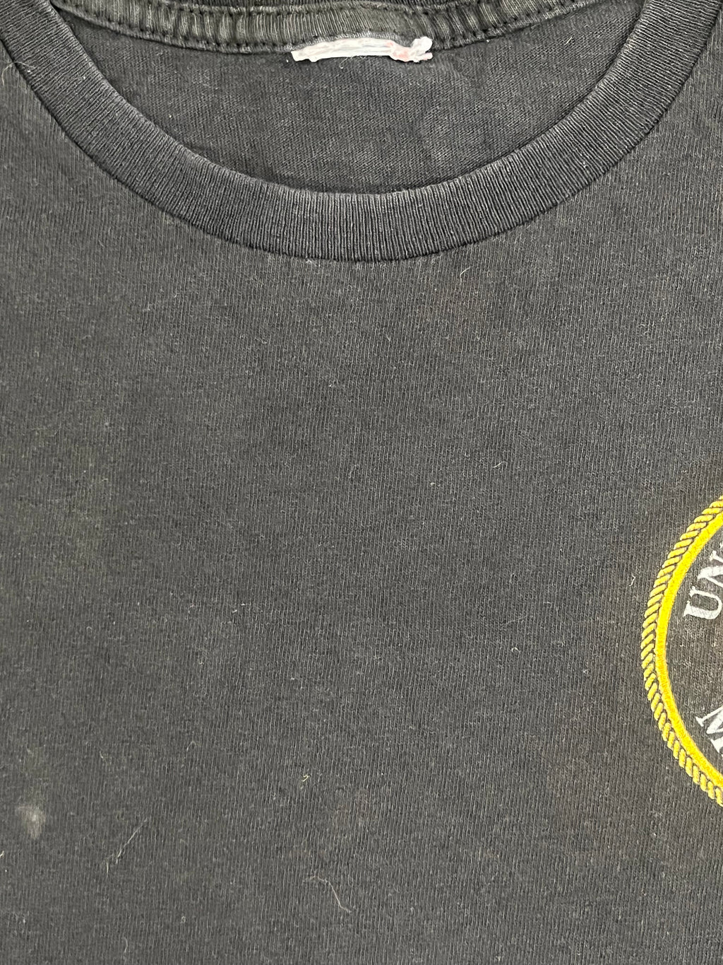Close-up of a dark gray heathered fabric surface with a partial yellow circular graphic at the top edge and a ribbed collar trim on the left side.