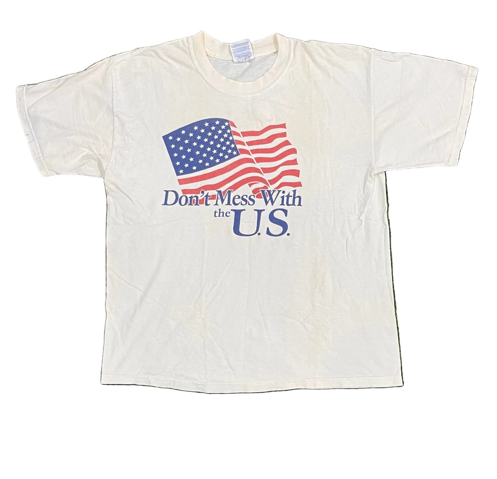 A white short-sleeve graphic t-shirt laid flat on white background The shirt features a printed waving American flag with the text 'Don't Mess With the U.