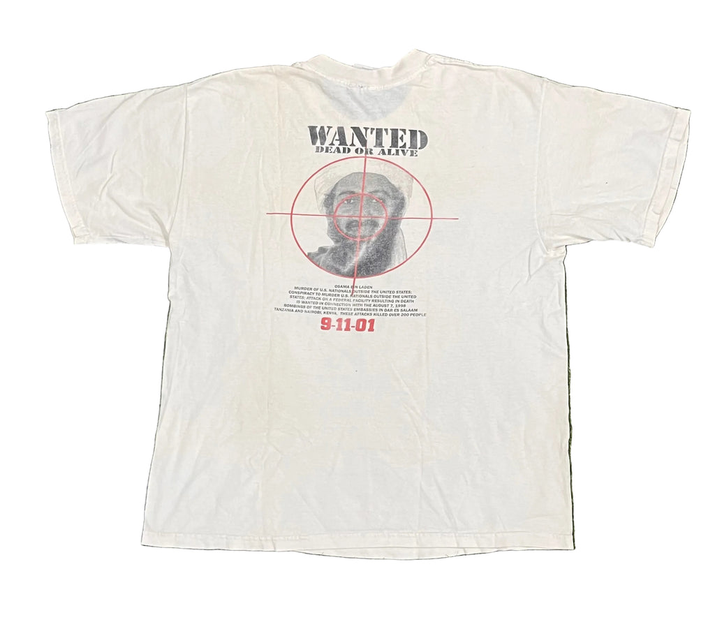A white short-sleeve graphic T-shirt laid flat on white background The back of the shirt features a distressed graphic with the word 'WANTED' above a portrait inside a red crosshair, with red text reading '9-11-01' below.