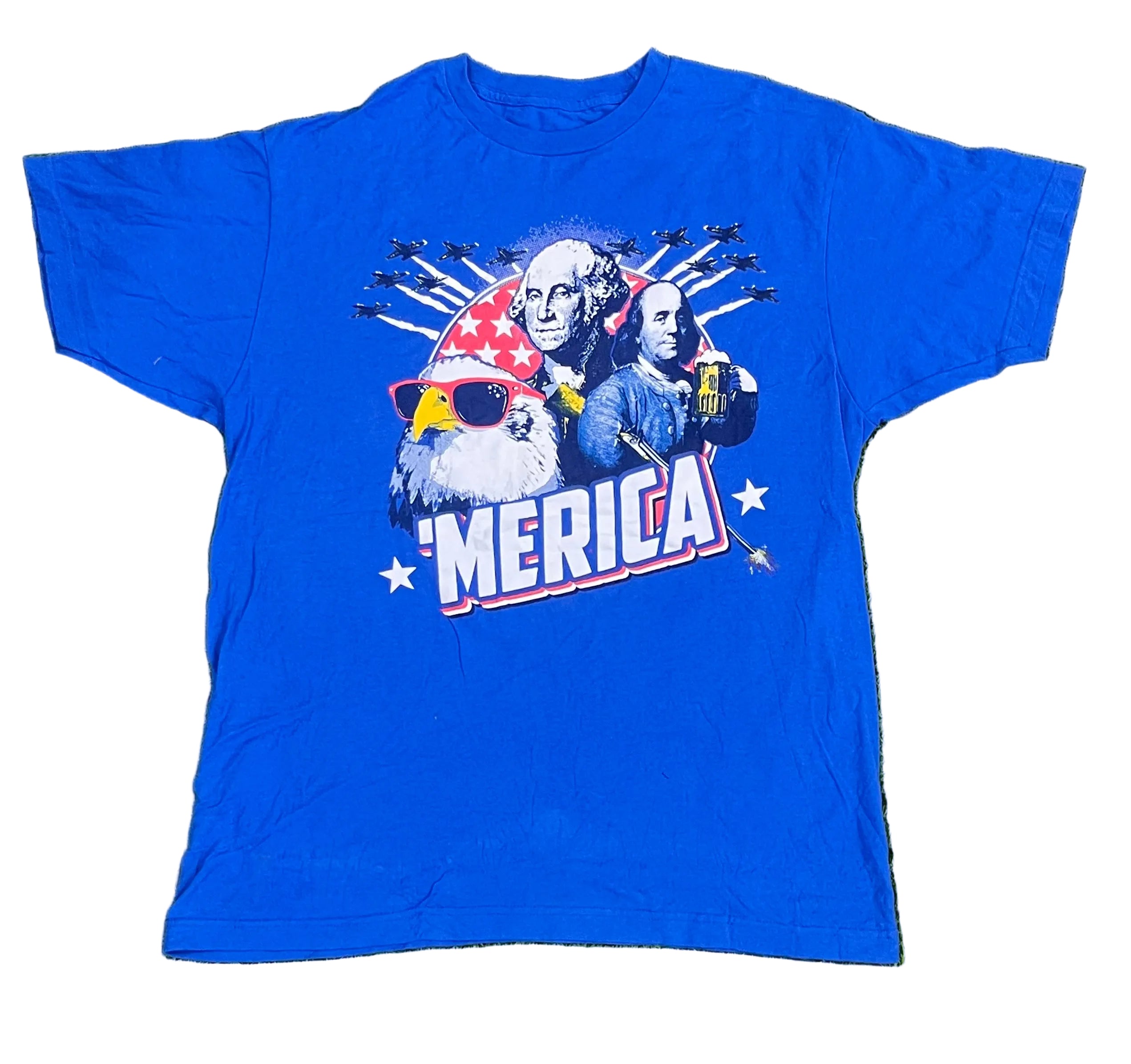 A royal blue short-sleeve graphic t-shirt laid flat on white background The front of the shirt features a patriotic graphic with George Washington, a bald eagle wearing a red and white star-spangled hat and yellow sunglasses, and the text 'AMERICA' in white with red and blue outlines.